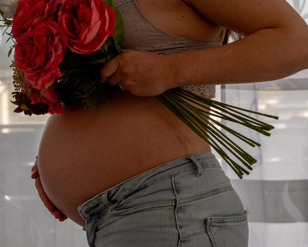 Ein Babybauch fotografiert, und drüber ist ein Blumenstrauß